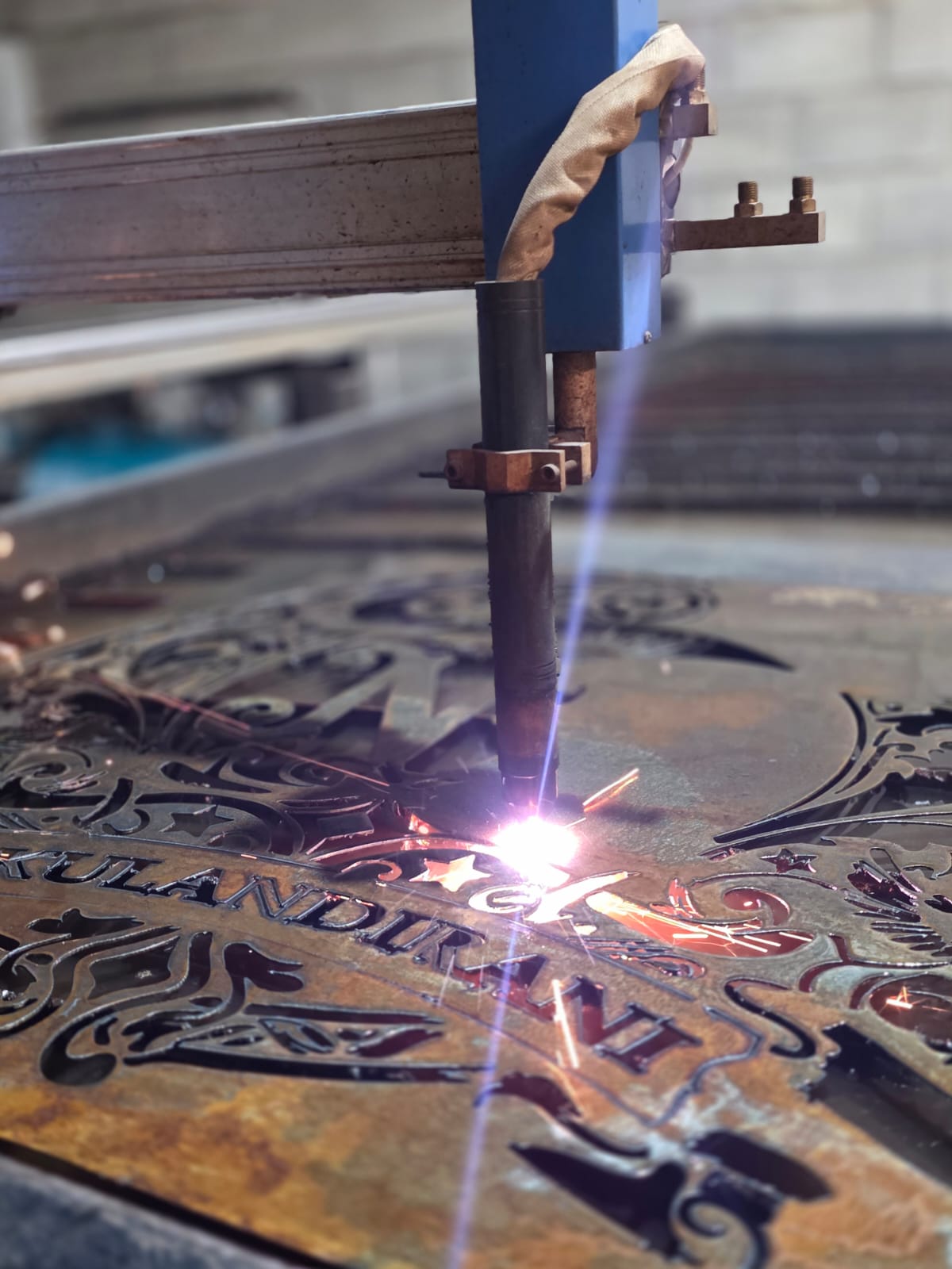Plasma torch cutting an ornate steel welcome sign with sparks flying