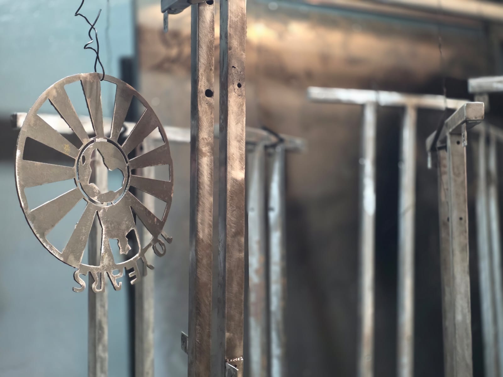 Laser-cut steel decorative sunburst piece hanging on the powder-coating line