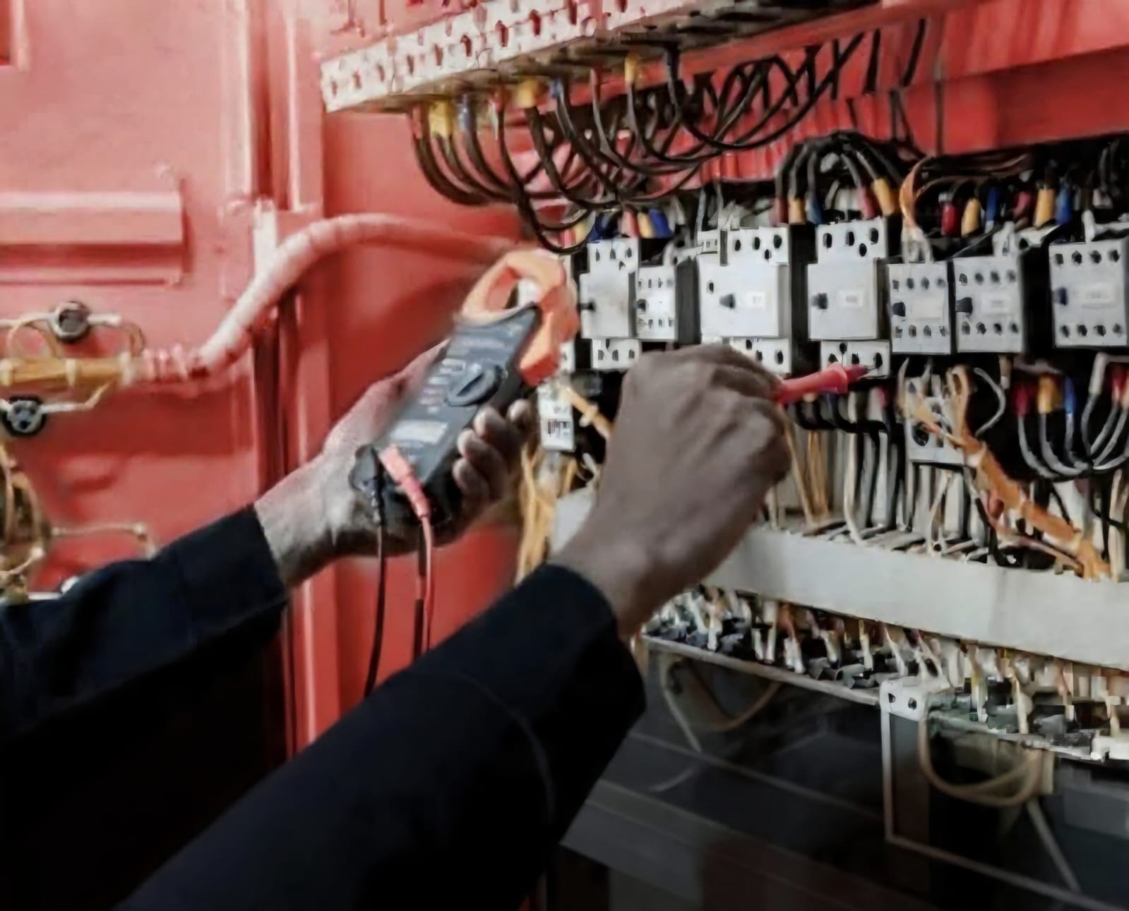 Technician testing an electrical control panel with a clamp meter
